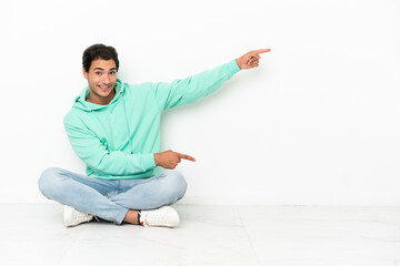 Caucasian handsome man sitting on the floor pointing finger to the side and presenting a product