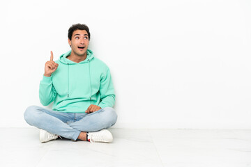 Caucasian handsome man sitting on the floor intending to realizes the solution while lifting a finger up