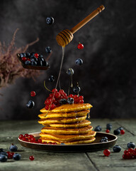 Homemade pancakes stack with fresh berries and honey on dark background, beautiful conceptual levitation studio picture, flying food art. Sweet pastry, copy space.