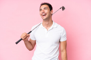 Young golfer player man isolated on pink background laughing