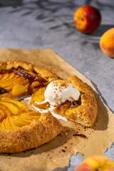 Peach galette with ice cream, homemade round  opened pie with summer fresh fruits, brown sugar, greens, Top view, sunny day, copy space. Homemade dessert on grey table, sweet pastry, French cuisine.
