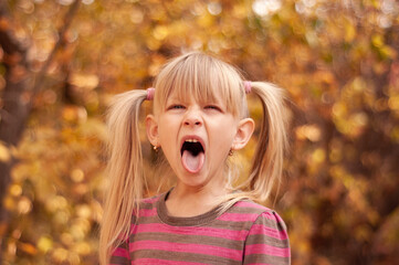 The child yawns. Portrait of a blonde girl in an autumn park.