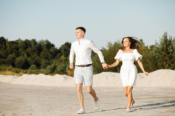 A happy couple is having fun running on the sand holding each other's hands.