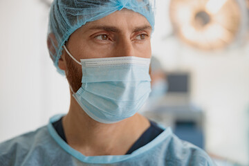 Close up of professional doctor in mask standing in operating room before surgery and looking away