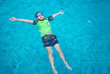 boy wearing a swimsuit and glasses swimming in the middle of the pool with a blue water background