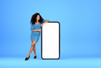 African woman pointing at big phone with empty display, blue background