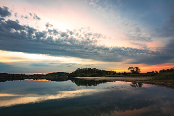 Epic red and gold clouds over forest lake at sunset. Dramatic cloud cover. Symmetrical reflections on the water, natural mirror. idyllic landscape.