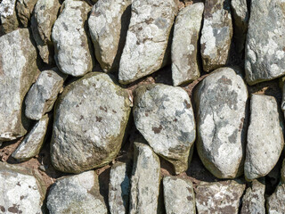 Masonry as a background. A fragment of a fence made of untreated stone blocks, texture. Gray and brown stones
