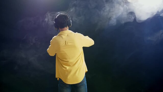 Back View Of A Young Boy With Headphone Holding A Microphone And Rapping On The White Smoke Black Background
