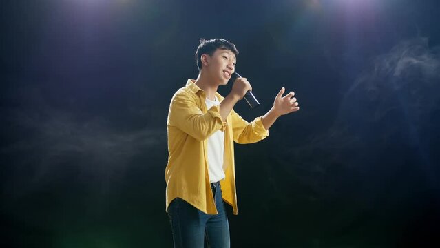 Young Asian Boy Holding A Microphone And Rapping On The White Smoke Black Background
