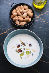 Bowl of ajoblanco or spanish white gazpacho served with grapes, high angle view on a dark-olive marble background, vertical shot