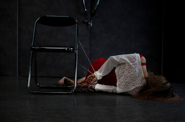hostage woman was being hands tied behind back and fell from a chair in dark room. concept of...