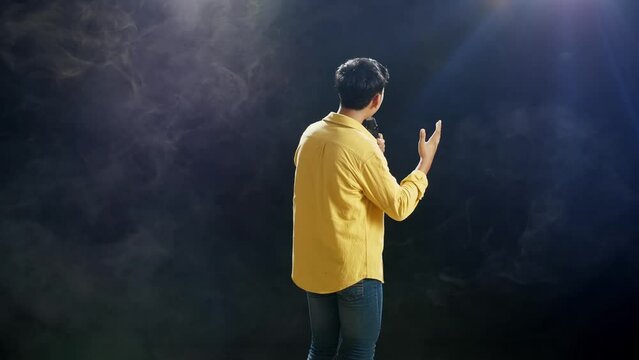 Back View Of A Young Boy Holding A Microphone And Singing On The White Smoke Black Background
