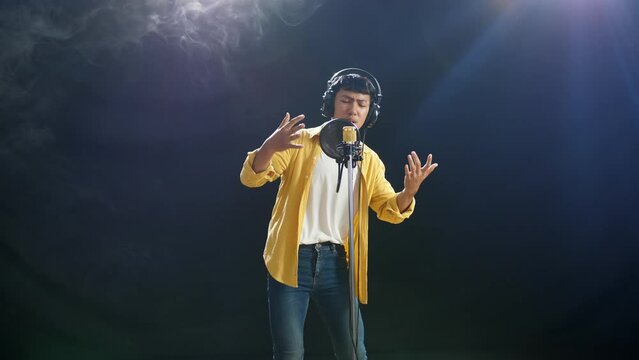 Young Asian Boy With Headphone Rapping Into A Condenser Microphone On The White Smoke Black Background
