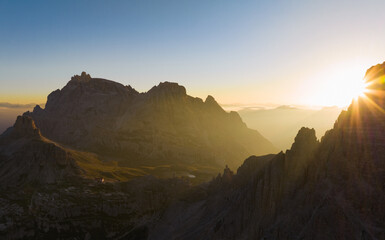 Fototapeta na wymiar View from above, stunning aerial view of a mountain range during a beautiful sunrise with a mountain hut in the distance. Tre Cime di Lavaredo, Dolomites, Italy.