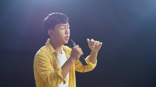 Young Asian Boy Holding A Microphone And Rapping On The Black Background
