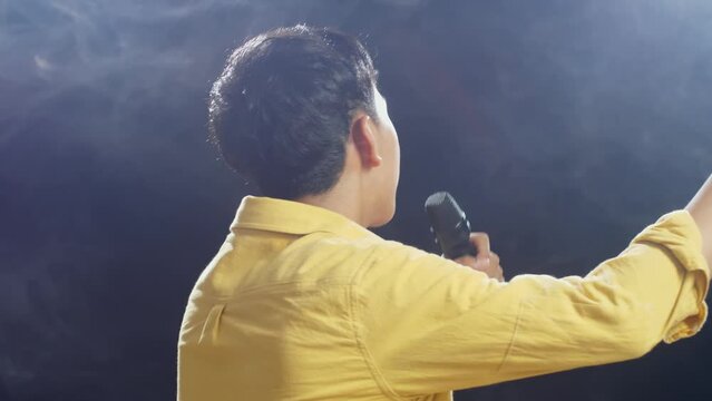 Close Up Back View Of Young Asian Boy Holding A Microphone And Rapping On The White Smoke Black Background
