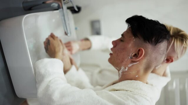 Gay couple in bathroom in the morning, washing face in front of mirror