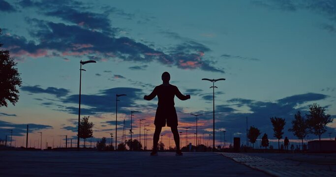 sportive man is rising hands up like winner, silhouette against beautiful sunset sky, 4K, Prores