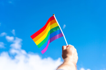 LGBT flag in hand against cloudy sky