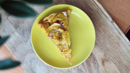 incredibly appetizing piece of apple pie on a wooden table with a plant in the background
