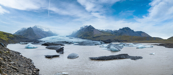 Glacier tongue slides from the Vatnajokull icecap or Vatna Glacier near subglacial Oaefajokull volcano, Iceland. Glacial lagoon with ice blocks and surrounding mountains.