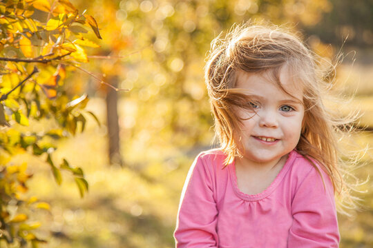 Young girl on a windy day smiling next to a deciduous tree