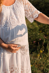 Against the background of pregnant woman's belly, the shadow of heart from her hands. Selective focus. Picture for articles about pregnancy, health, women.