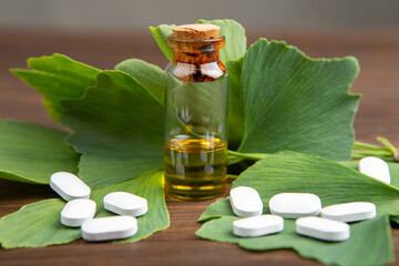 Bottle of essential oil, pills and ginkgo biloba leaves on wooden background. Traditional, herbal medicine and Homeopathy concept.