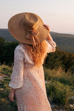 Woman holds hat in her hand and looks at nature in sunset light. Selective focus. Picture for articles about women, success, psychology.