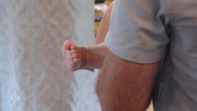 The man holds the baby in his arms. Baptism of the baby in the church. Close-up of baby's feet