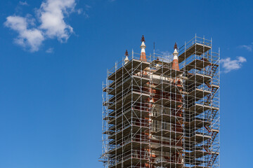 Looking up at a church steeple surrounded buy construction scaffolding against a blue sky