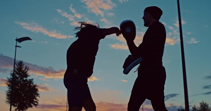two sportsmen are training boxing punches outdoors, silhouette against beautiful sky, 4K, Prores