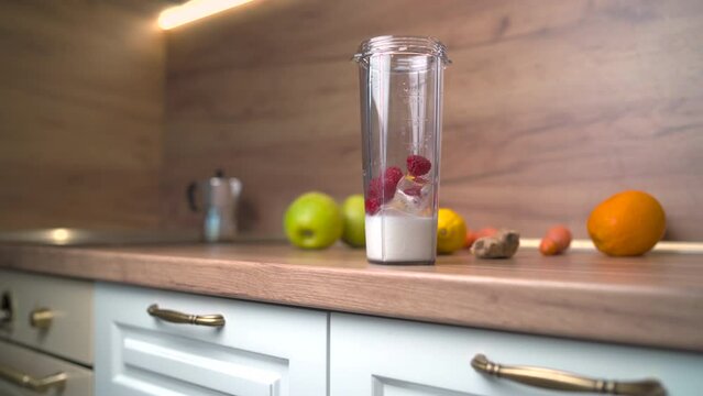 Blender cup on wooden counter. Raspberries falling in milk for smoothie