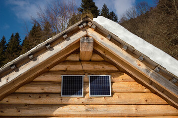 Conceptual image. Detail of a wooden house with small solar panels under the roof.