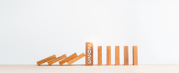 The 2023 year numbers calendar on wooden cube blocks stops falling blocks and collapsing dominoes on table isolated on white background. Preventing the domino effect and staying strong concept banner.