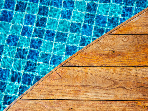 Top view of empty wooden plank table or deck floor curved shape in front of the blurred background of blue mosaic tiles grid pattern in swimming pool. Empty space on poolside, summer background.