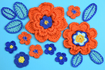 Beautiful crocheted orange roses and blue leaves on a blue paper background.

