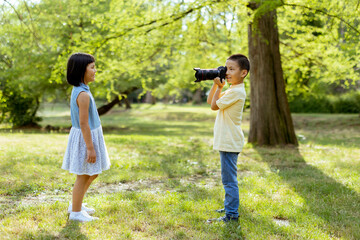 Little asian boy acting like a professional photographer while taking photos of his little sister