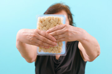 A woman holds a package of uncooked fresh gnocchi package on a blue background. Nutrition. Pile....