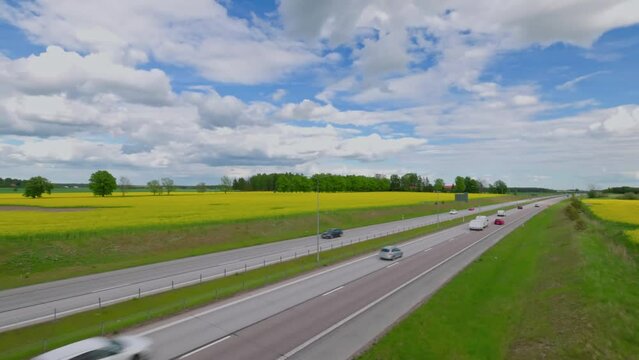 Beautiful top view of highway with moving cars. Rapeseed fields with white clouds against sky. Sweden.