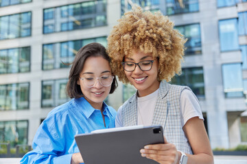 Creative female designers use digital tablet for productive work focused at screen work out plan together pose against blurred modern urban building. People cooperation and coworking concept
