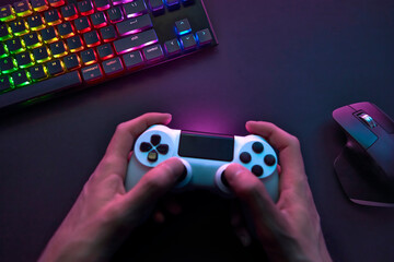 High angle view of male hand using game controller above dark desk with computer input devices.