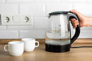 A man makes tea using boiling water from an electric kettle in the kitchen at home. It's time to...