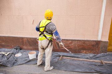 A rear view of a painter in a helmet painting a wall, with a paint roller and a bucket