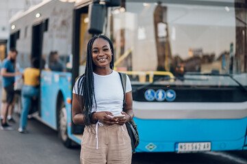 African american woman using smartphone and standing in front of a bus