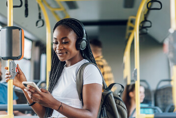 African american woman riding a bus and using a smartphone and headphones - obrazy, fototapety, plakaty