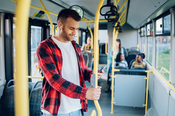 Man is riding in a bus and using a smartphone while holding for a bar