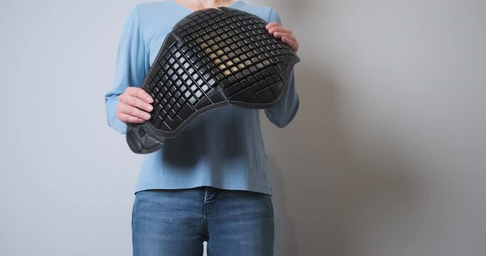Woman holds in her hands a motorcycle back protection for a jacket. Hands crumpling a plastic shield. Front view, demonstration of a motorcycle accessory for protection.