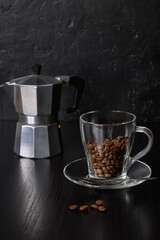 Coffee beans in glass cup and a coffee maker on a dark background